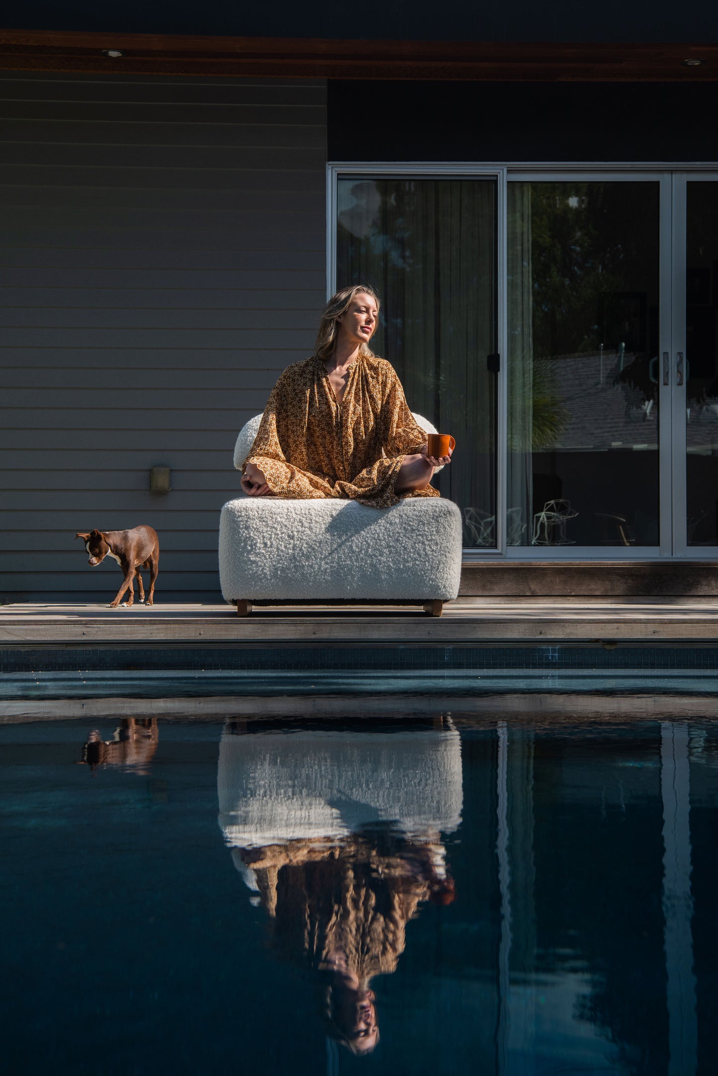 Women Sitting on Meditation Chair by Rue and Williams Home at private residence with a pool and dog standing beside her.  Woman is in mediation pose. Modern design with no arms and a curved back, perfect for enhancing mindfulness practices and adding tranquility to any space.