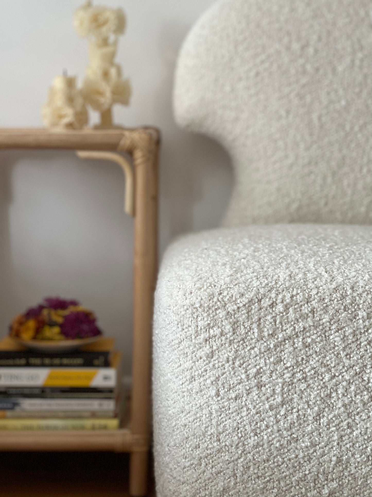 Close up of Salt-colored bouclé Meditation Chair by Rue and Williams Home. Modern design with no arms and a curved back, perfect for enhancing mindfulness practices and adding tranquility to any space. with table of objects next to it.